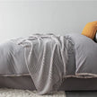 Gray textured blanket draped over a bed with a yellow pillow.