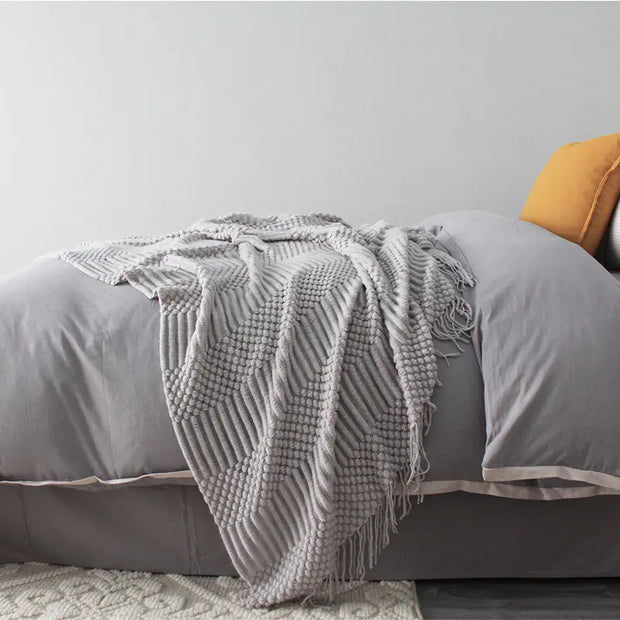 Gray textured blanket draped over a bed with a yellow pillow.