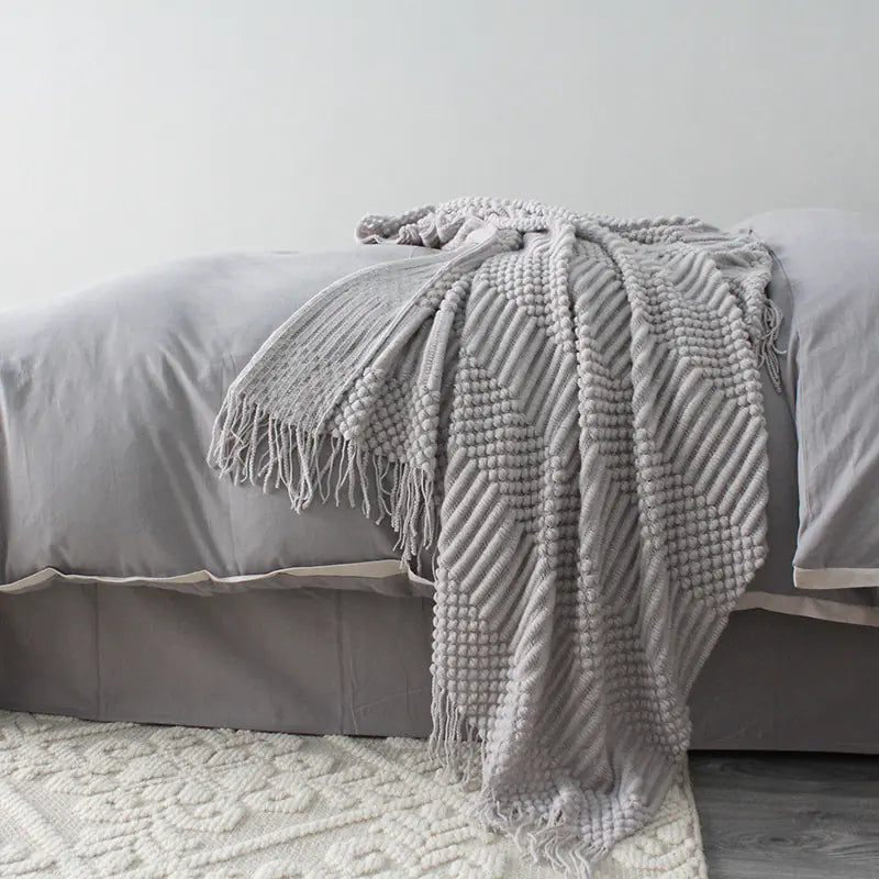 Gray textured blanket draped over a bed with a neutral background