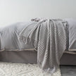 Gray textured blanket draped over a bed with a neutral background