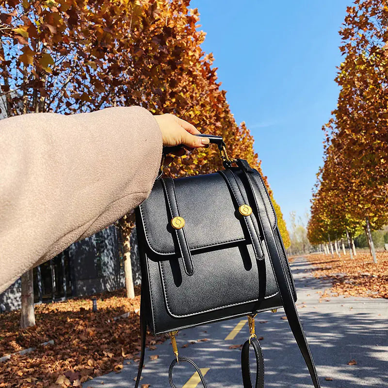 Person holding a black handbag with gold accents in an autumn setting