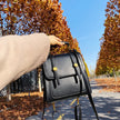 Person holding a black handbag with gold accents in an autumn setting