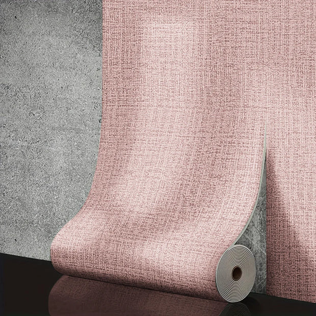 Roll of pink textured wallpaper against a gray concrete wall.
