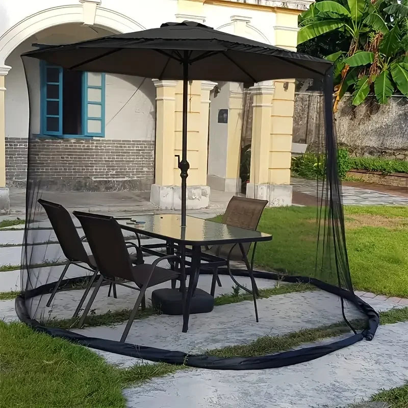 Outdoor patio set with table and chairs under a large black umbrella in a garden setting.