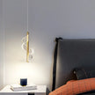 Modern pendant light hanging above a bed with a nightstand in a bedroom setting.