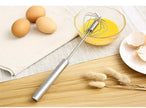 Metal whisk next to eggs and a bowl of whisked eggs on a wooden surface.