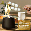 Person roasting marshmallows over a small fire pit on a table with food and a mug.