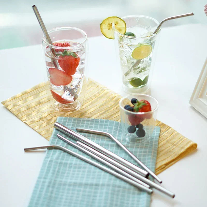 Two glasses of water with fruit and metal straws on a table with a napkin and small bowl of berries.