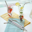 Two glasses of water with fruit and metal straws on a table with a napkin and small bowl of berries.