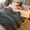 Woman lying on a bed under a dark gray blanket in a cozy bedroom setting.