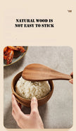 Hand using a wooden spoon to serve rice from a bowl on a textured surface.