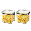 Two glass storage containers with lids filled with yellow cereal on a white background