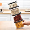 Stack of clear containers with black lids filled with various foods on a kitchen counter.