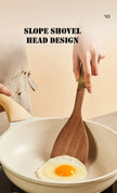 Wooden spatula being used to cook an egg in a white pan with text 'Slope Shovel Head Design'.