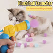 Cat playing with a plush ball launcher and colorful balls on a light background