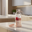 Glass bottle with pink base and lid, containing ice and raspberries, on a white background.