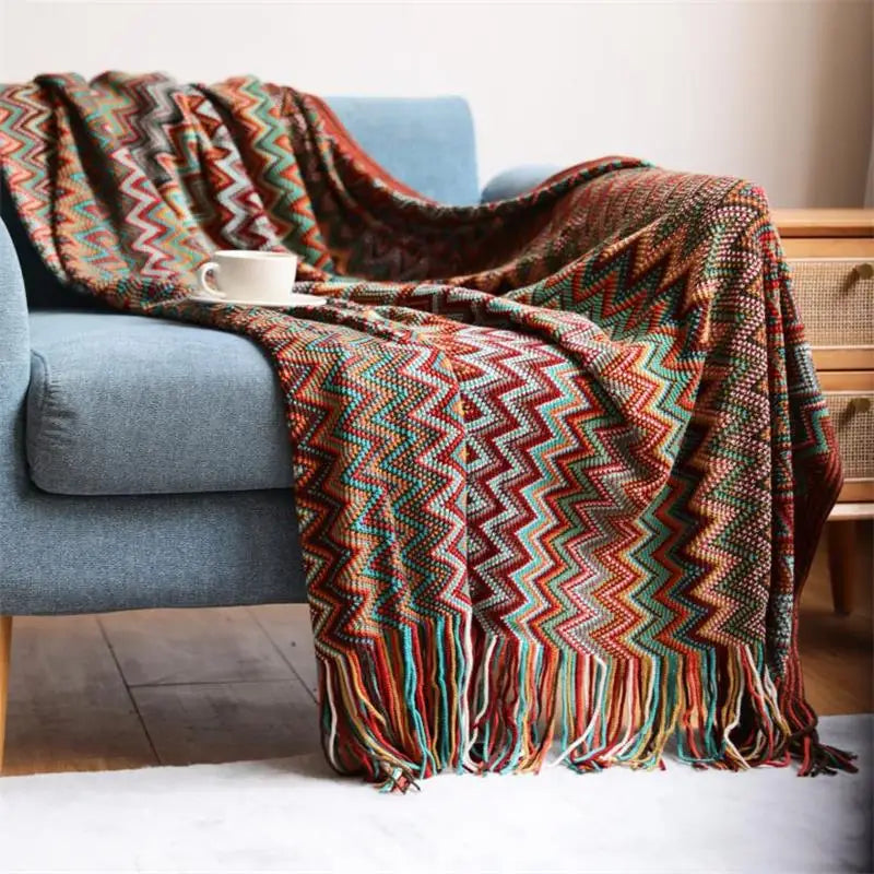 Colorful zigzag patterned throw blanket draped over a blue sofa with a cup on a table.