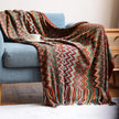 Colorful zigzag patterned throw blanket draped over a blue sofa with a cup on a table.
