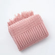 Pink textured blanket with fringe on a white background