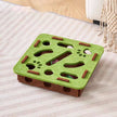 Green and brown puzzle toy for pets on a striped carpet