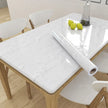 Dining table with marble-patterned tablecloth and roll of tablecloth on a wooden floor.