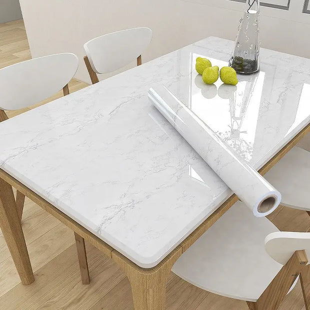 Dining table with marble-patterned tablecloth and roll of tablecloth on a wooden floor.