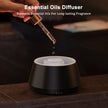 Essential oils being dripped into a black essential oils diffuser on a dark surface.