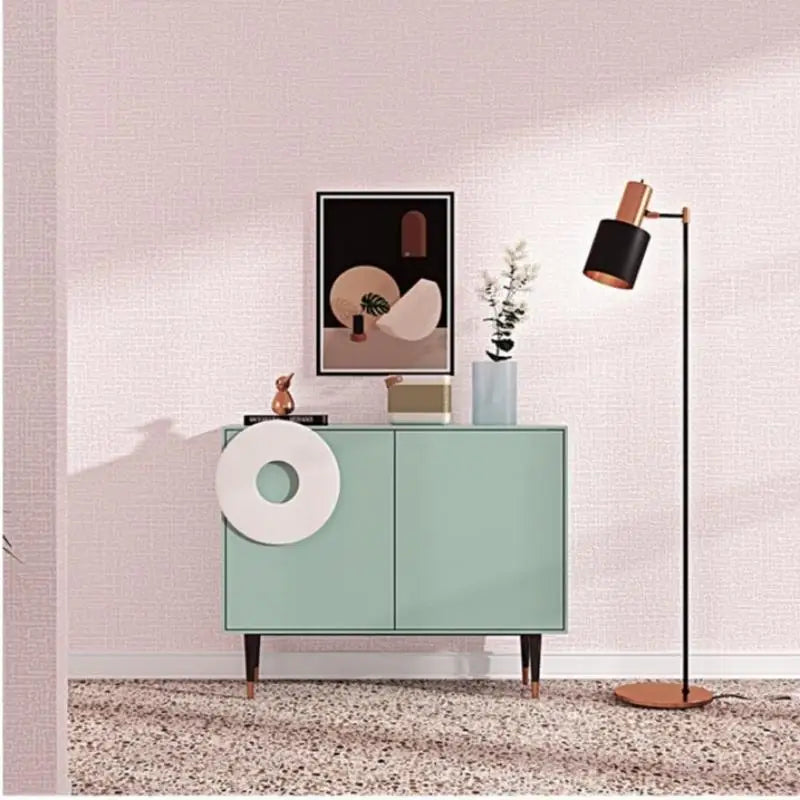 Modern interior with a green cabinet, floor lamp, and abstract art on a light pink wall.