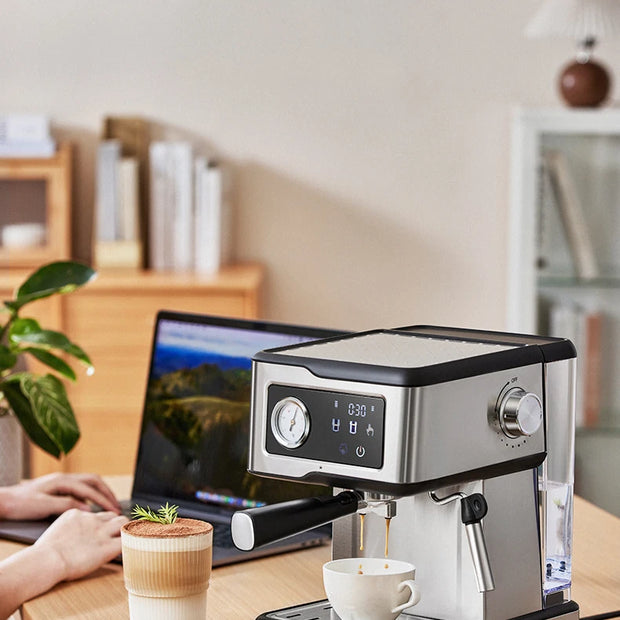 Espresso machine on a wooden desk with a laptop and coffee cup in a home office setting.