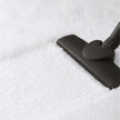 Black vacuum cleaner head cleaning a white textured surface