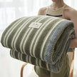 Person holding a striped blanket with a visible brand label against a blurred background