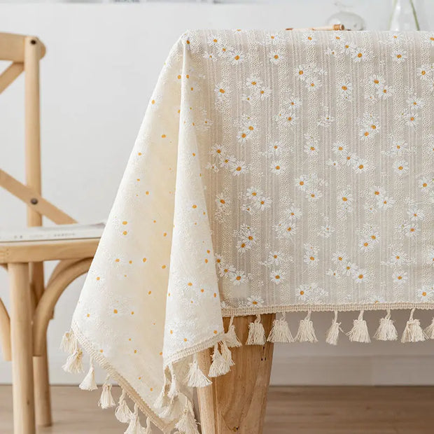 Beige tablecloth with floral pattern and tassels on a wooden table