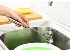 Hand washing a metal whisk in a kitchen sink with soap and water.