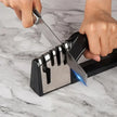 Person sharpening a knife using a black and silver knife sharpener on a marble surface.