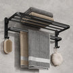 Black towel rack with folded towels and bath accessories on a gray wall.