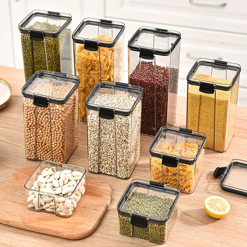Set of clear kitchen storage containers with black lids on a wooden surface.