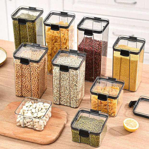 Set of clear kitchen storage containers with black lids on a wooden surface.