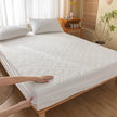 White mattress cover being fitted onto a bed in a bedroom setting.