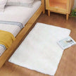 White fluffy rug on a wooden floor next to a bed with a wooden headboard.