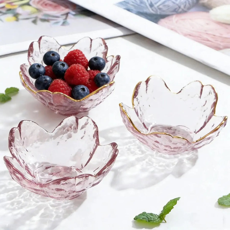 Three pink glass bowls with gold rims, one filled with berries, on a white surface.