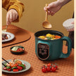 Person using a wooden spoon to serve food from a green electric pot on a table with plates and vegetables.