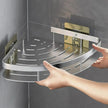 Corner shower caddy being held by a hand against a gray tiled wall.