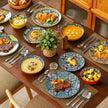 Dining table set with colorful plates, bowls, and utensils on a wooden table.
