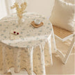 Round table with floral tablecloth, cup, and decorative items in a cozy room.