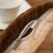 Close-up of a brown plush blanket with a zipper, blurred white cup in the background