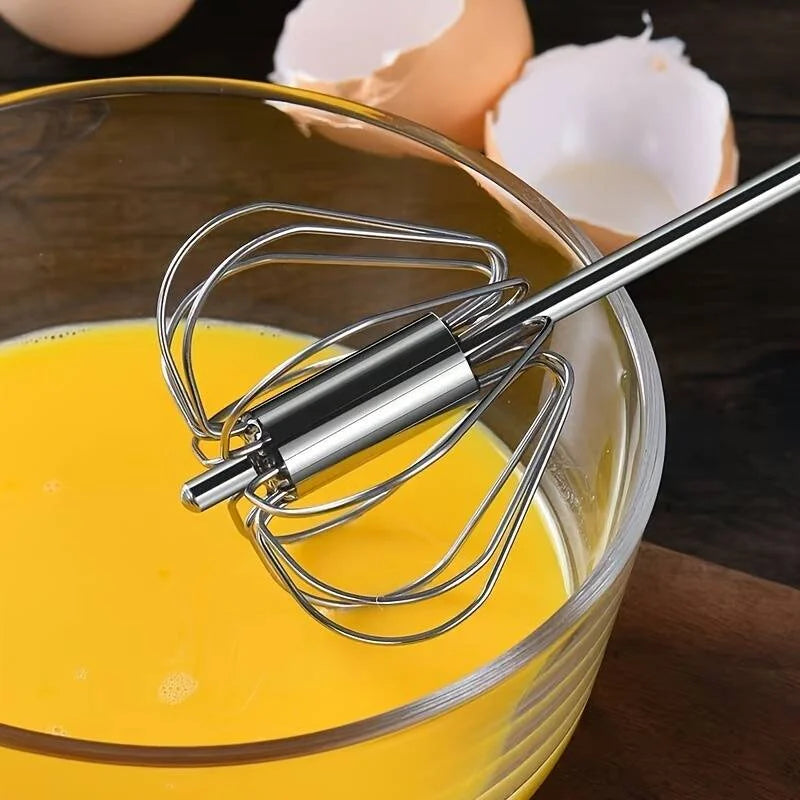 Metal whisk in a bowl of yellow liquid with eggshells in the background