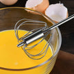 Metal whisk in a bowl of yellow liquid with eggshells in the background