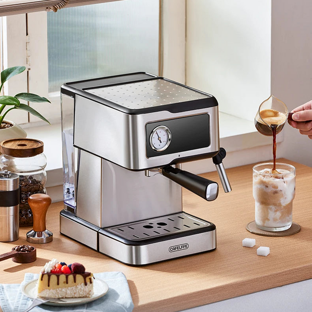 Espresso machine on a kitchen counter with a glass of coffee and a small cake.