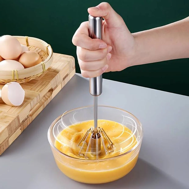 Hand using a hand mixer to blend eggs in a glass bowl on a kitchen counter.