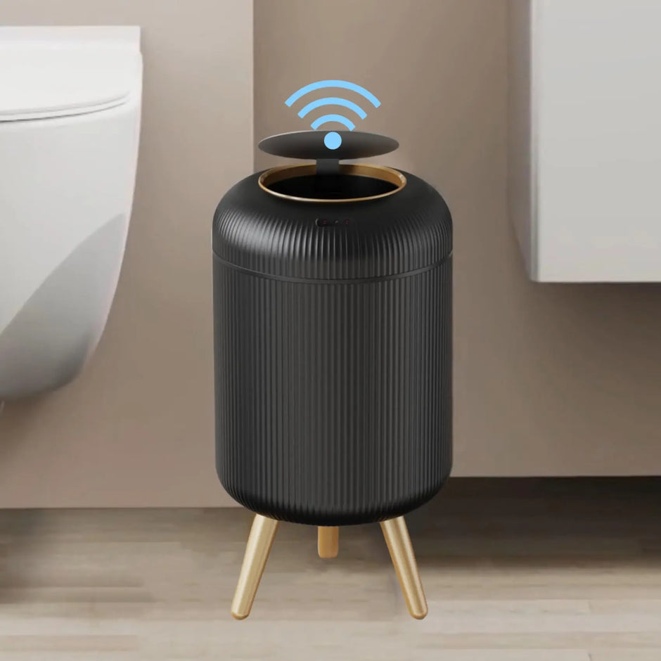 Black cylindrical device with gold legs on a wooden floor against a beige wall.